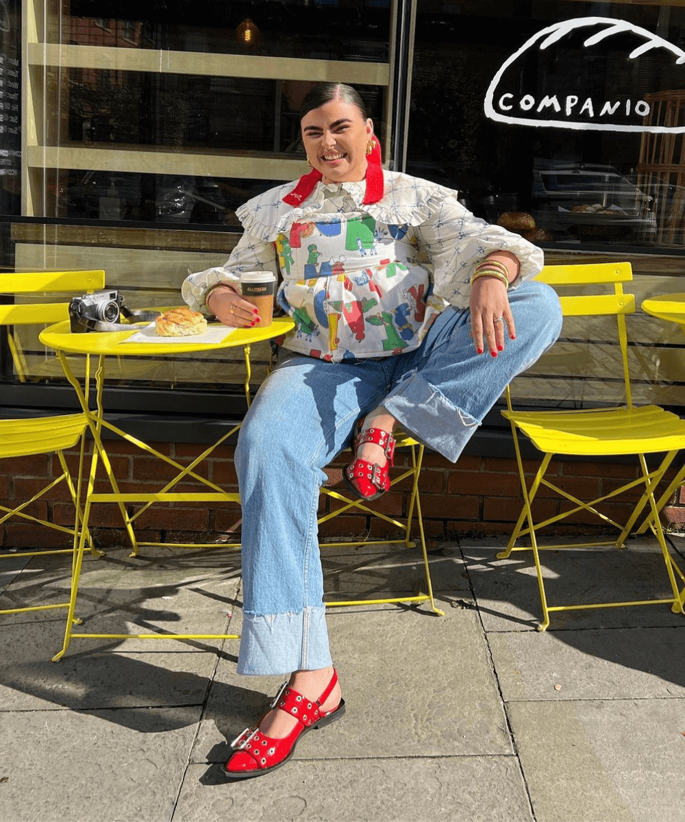 Francesca Perks - calça jeans, blusa colorida estampada e sapatilha vermelha de fivelas - sapatos tendência - inverno - mulher loira sentada na rua sorrindo - https://stealthelook.com.br