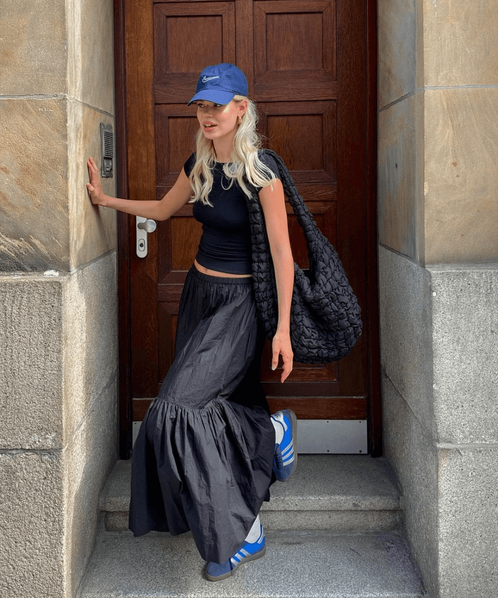 @linda.sza - saia midi preta, top preto, tênis e boné azul - tendências do verão - verão - mulher loira em pé na rua usando boné e óculos - https://stealthelook.com.br