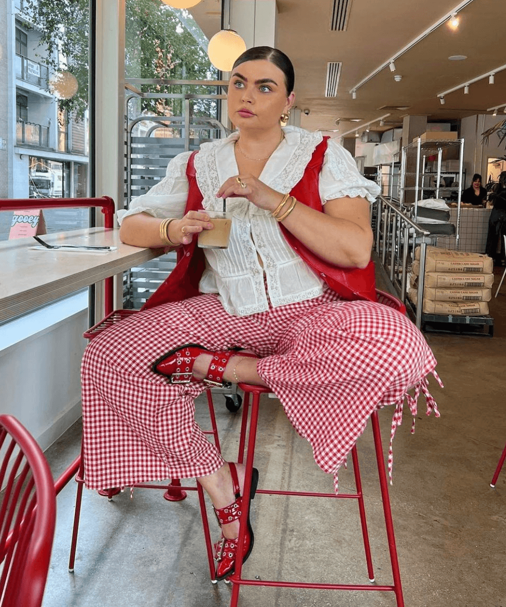 Francesca Perks - calça xadrez, blusa gola branca boneca, sapatilha vermelha - cool girls - verão - mulher loira sentada em um banco com uma das pernas cruzadas - https://stealthelook.com.br
