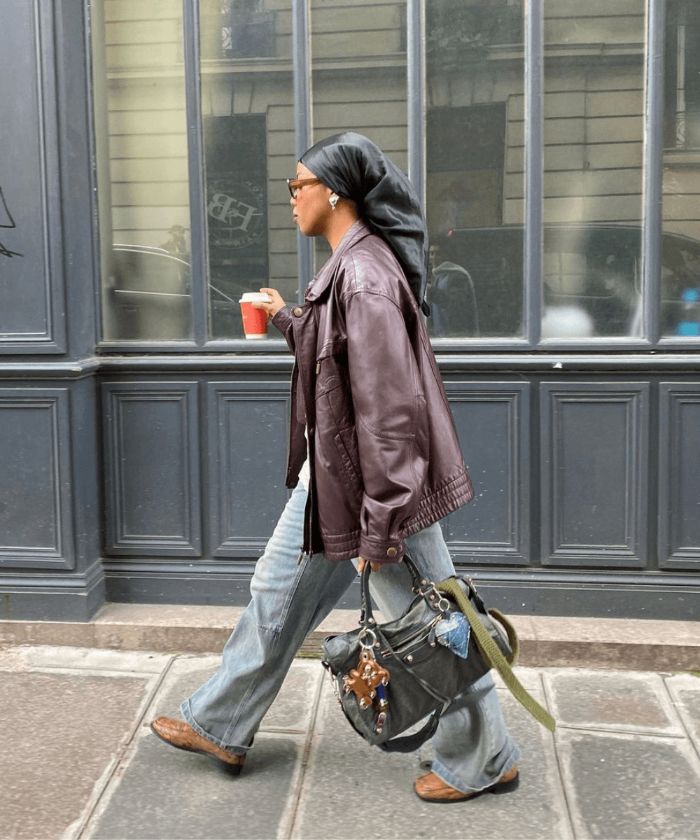 @blackmaroccan - calça jeans, jaqueta de couro marrom e bolsa com charms - bolsas tendência - inverno - mulher negra em pé na rua usando óculos de sol - https://stealthelook.com.br