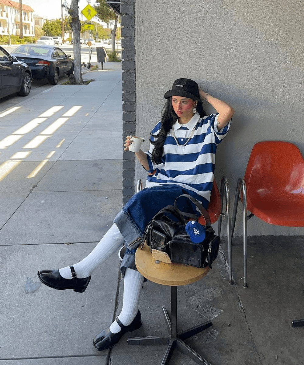 Ines Silva | @irisloveunicorns - bermuda jeans, blusa listrada azul e branca, boné e tênis - bolsas tendência - primavera - mulher sentada em um café na rua - https://stealthelook.com.br
