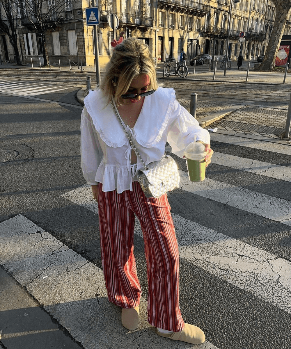 Chloé Allain - calça listrada, blusa de babados e tênis - calças estilosas - verão - mulher loira andando na rua usando óculos de sol - https://stealthelook.com.br