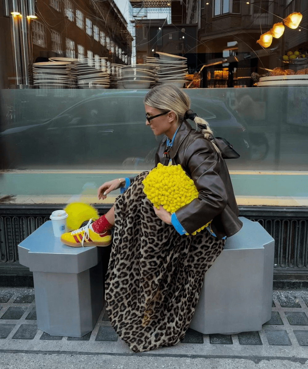 Olivia Anna-Catharina T - saia de oncinha, jaqueta, camisa azul e tênis amarelo - saia midi de oncinha - inverno - mulher loira sentada em um banco na rua - https://stealthelook.com.br
