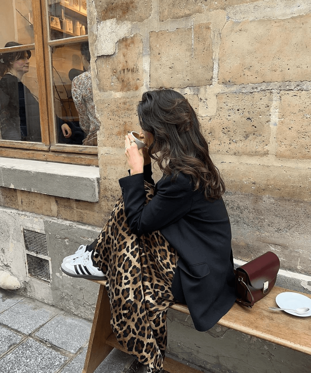Taïna Cassagnes - saia midi de oncinha, blazer preto e tênis - saia midi de oncinha - outono - mulher morena sentada em um banco na rua - https://stealthelook.com.br