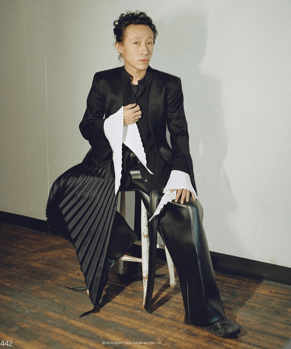 Robert Wun - calça preta, blusa branca e jaqueta preta - Designers asiáticos - inverno - homem asiático sentado em uma cadeira - https://stealthelook.com.br