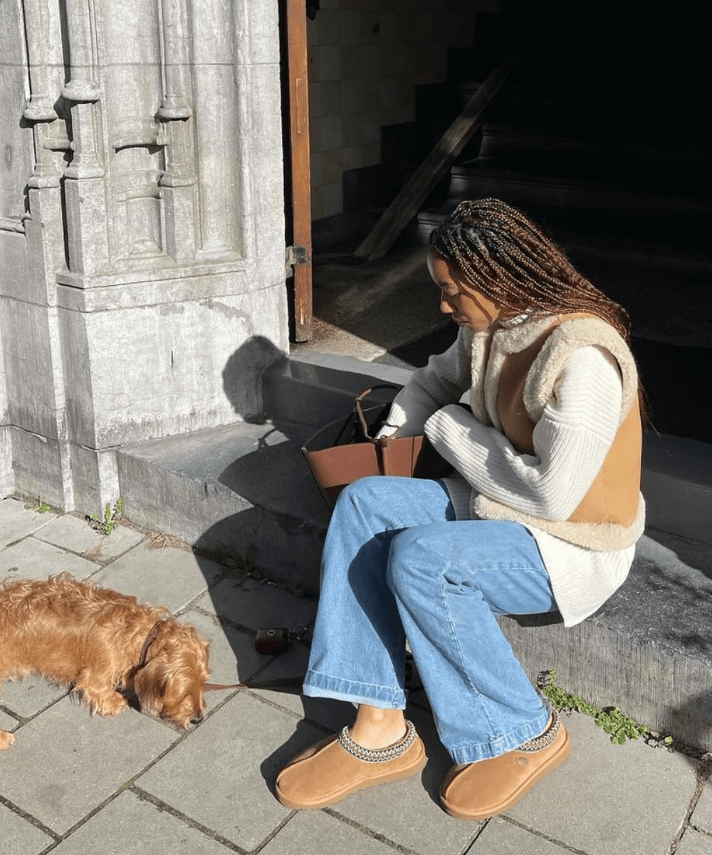 Amaka Hamelijnck - calça jeans, tricot, colete de pelúcia e tênis - looks de frio - inverno - mulher negra sentada na rua ao lado de um cachorrinho - https://stealthelook.com.br