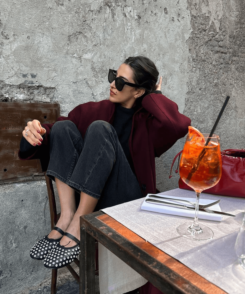 Taïna Cassagnes - tricot vermelho, calça preta e sapatilha preta com brilhos - looks red cherry - inverno - mulher usando óculos de sol sentada em uma mesa com as pernas dobradas - https://stealthelook.com.br