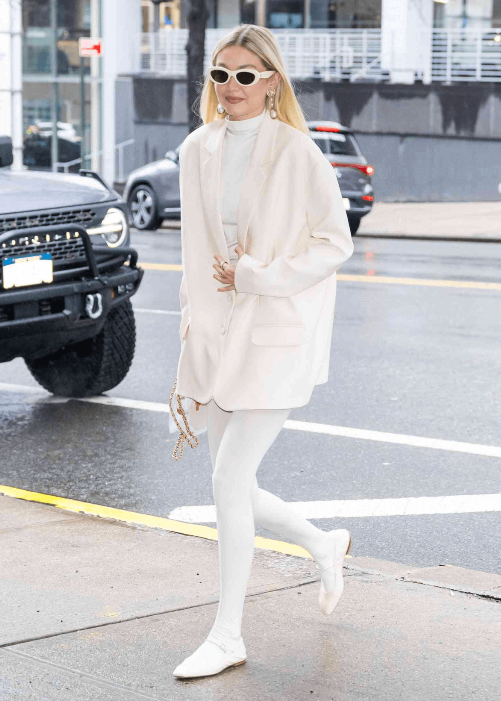 Gigi Hadid - look inteiro branco com blazer, meia-calça e sapatilha - meia-calça branca - inverno - mulher loira de óculos em pé na rua - https://stealthelook.com.br