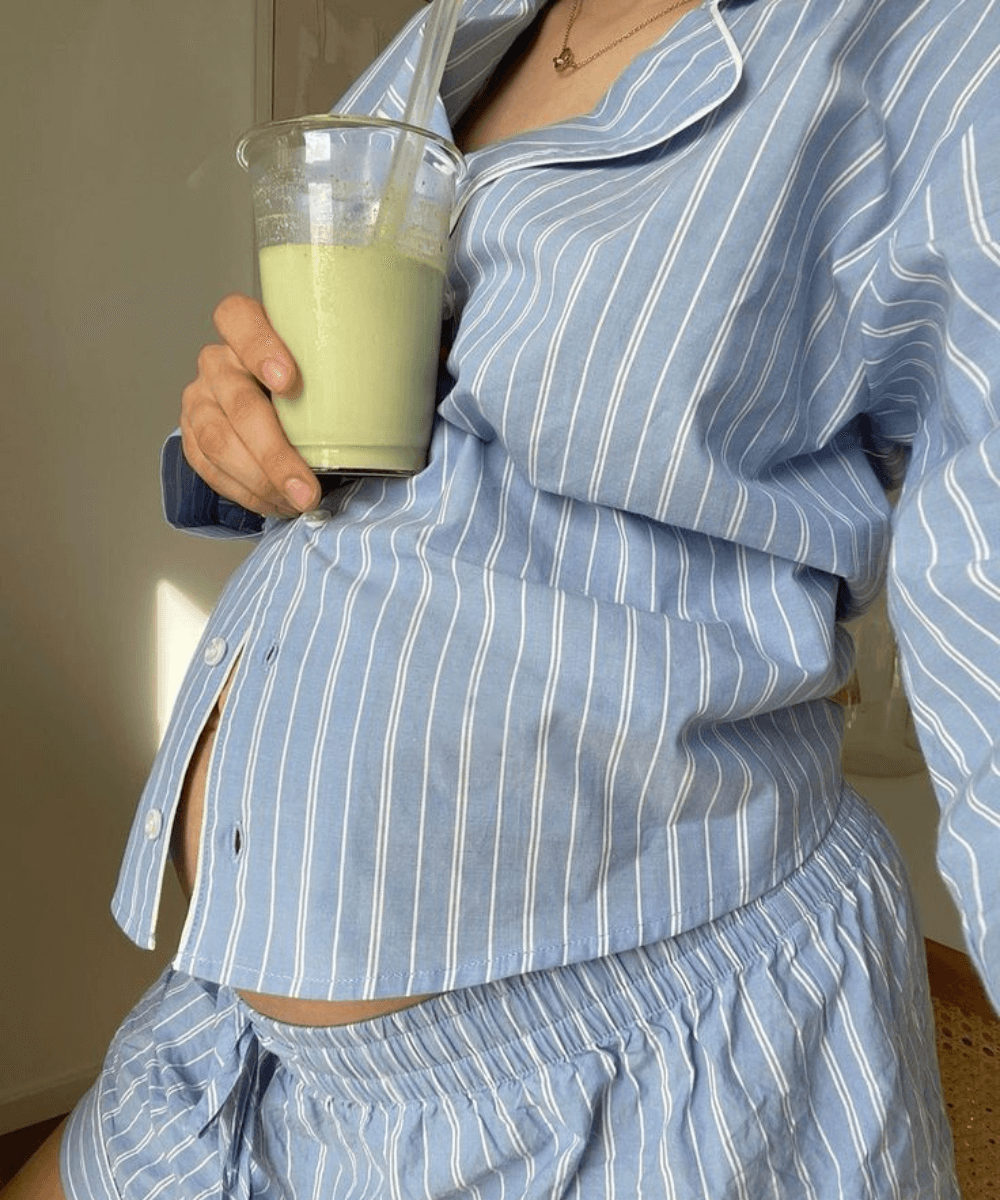 Ozempic x Fertilidade - pijama listrado azul - Ozempic - verão - mulher grávida em pé bebendo um suco verde - https://stealthelook.com.br