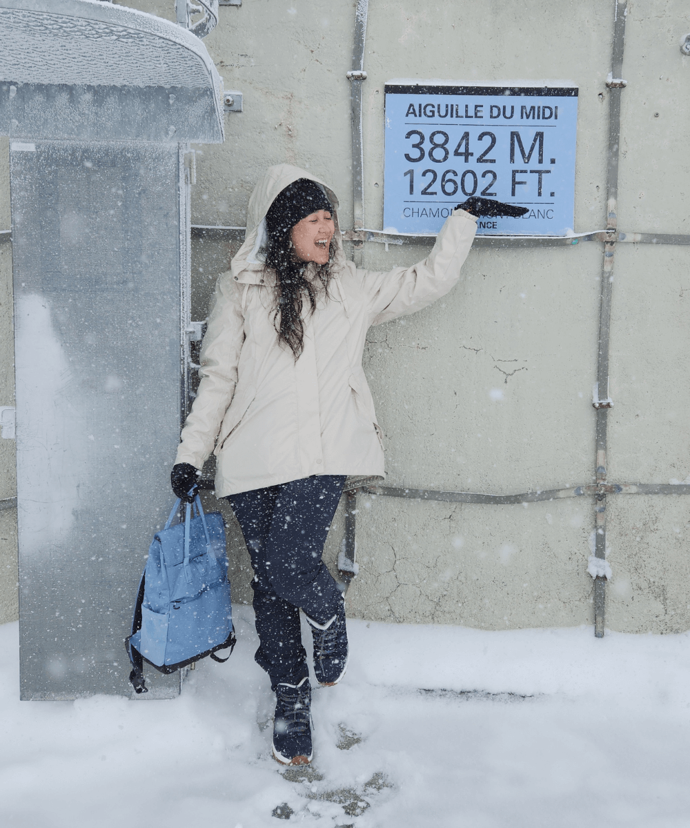 Iza Suzuki - roupa de neve - neve - inverno - mulher em pé apontando para uma placa que mostra 