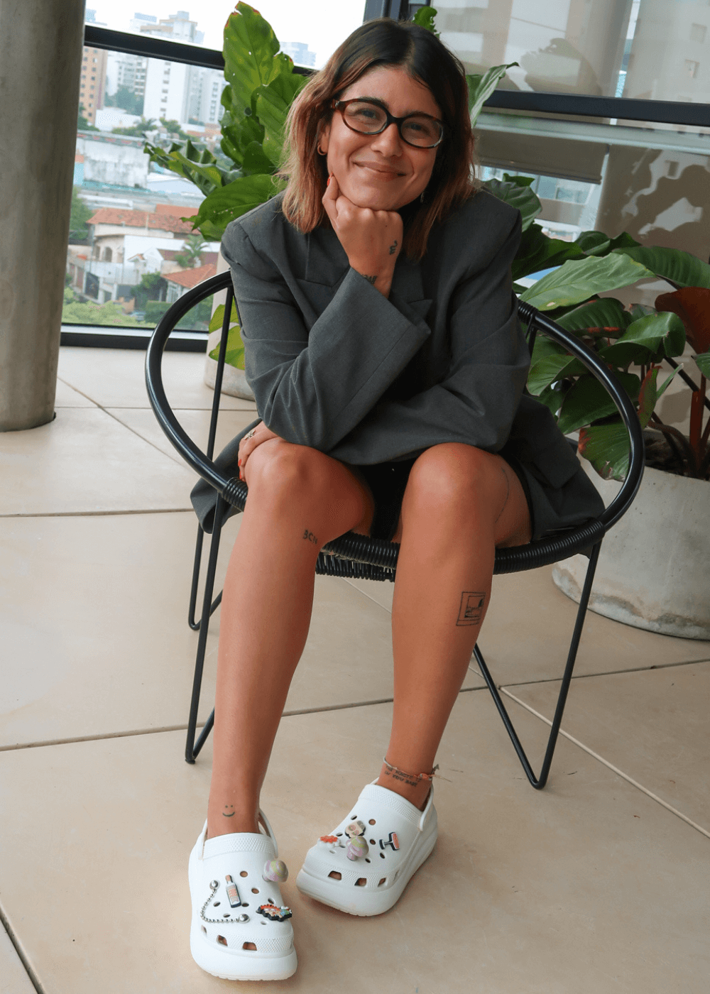 Thais Saviani Bastos - bermuda, camisa e crocs branco - sapato personalizado - outono - mulher de óculos sentada em uma cadeira sorrindo - https://stealthelook.com.br