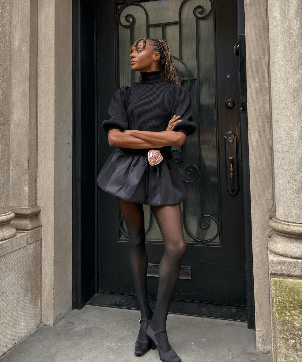 Camri Hewie - minissaia preta balonê, blusa preta, meia-calça e sandália preta - balonê - inverno - mulher negra em pé na rua - https://stealthelook.com.br