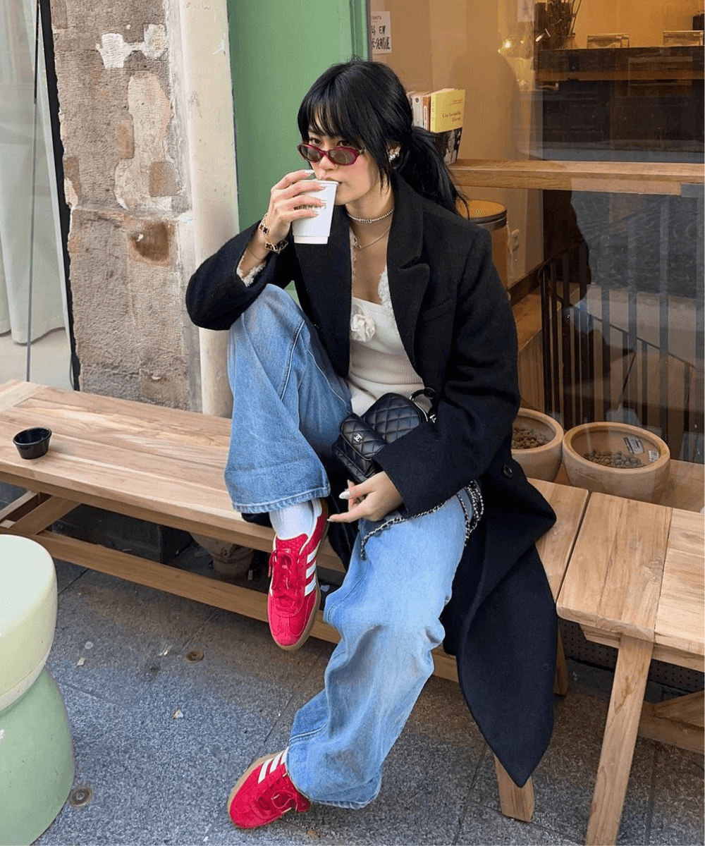 Jihoon Kim - calça jeans, tênis adidas vermelho, casaco preto e blusa branca - Adidas - outono - mulher asiática sentada em um banco na rua usando óculos de sol - https://stealthelook.com.br