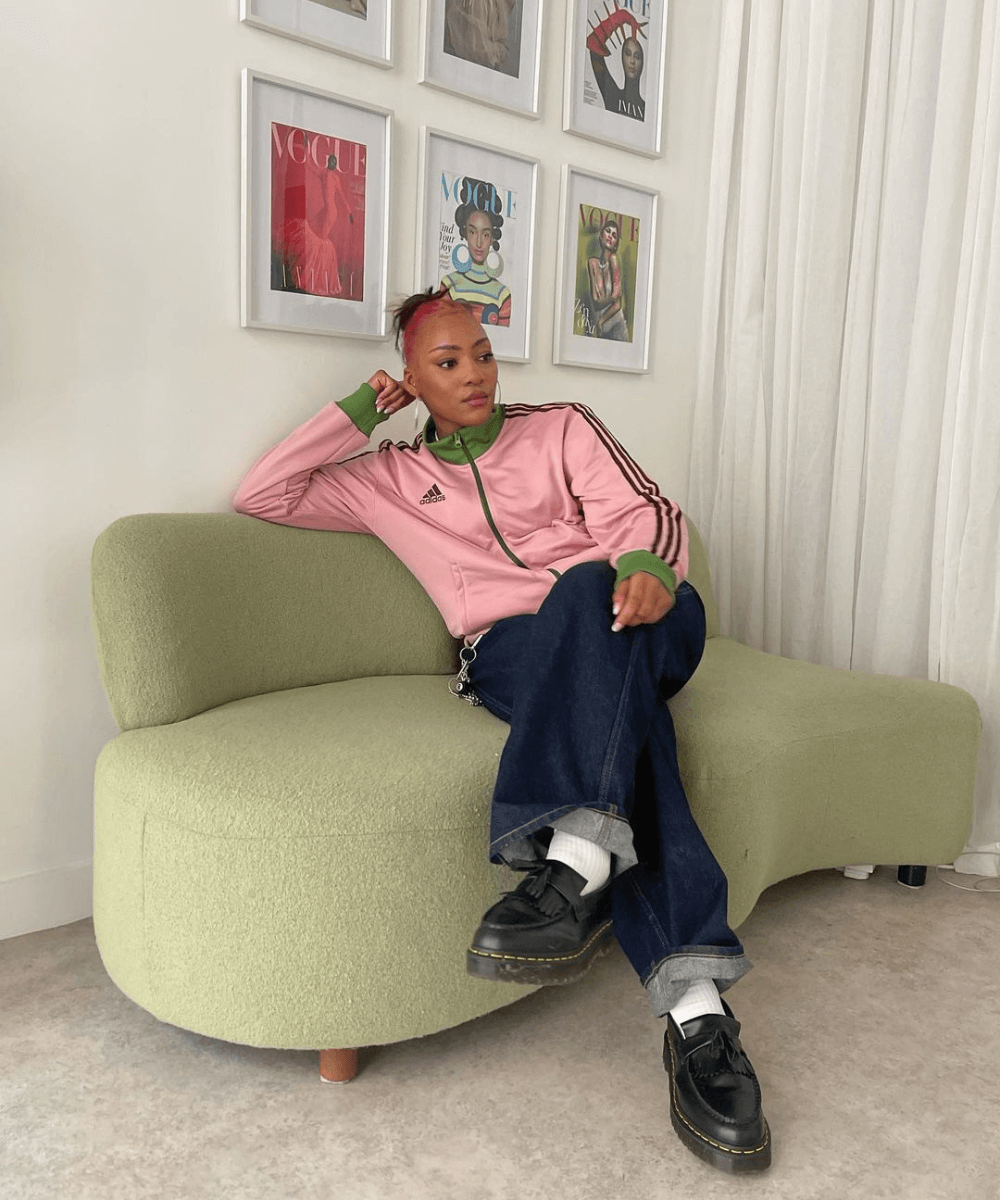 Belinda Ingrid | @toastedbananabread_ - calça jeans, jaqueta rosa adidas e mocassim - Adidas - outono - mulher negra sentada em um sofá - https://stealthelook.com.br
