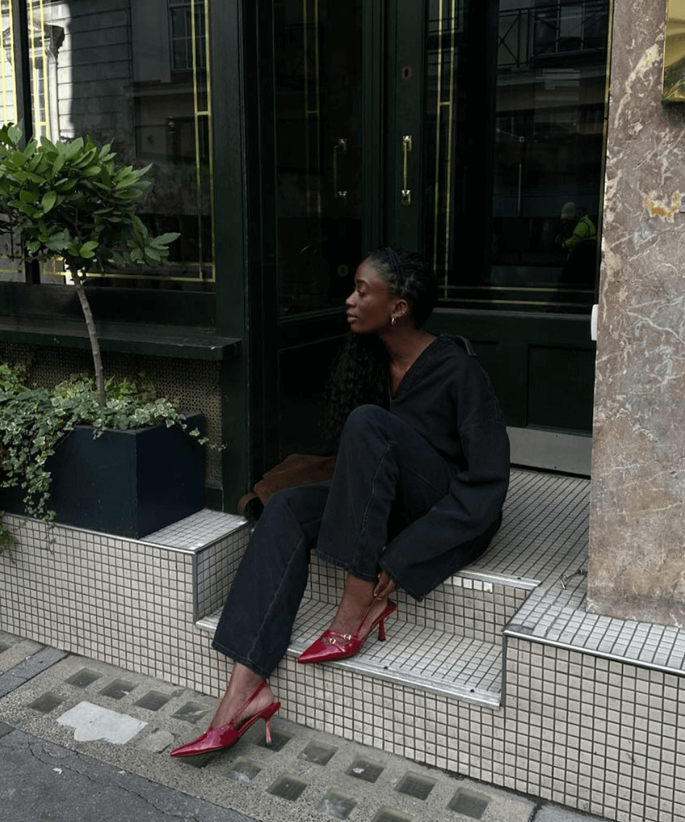 Liv Madeline - calça preta, camisa preta manga longa e slingback vermelho de tiras - outono 2024 - outono - mulher negra sentada em uma escada na rua - https://stealthelook.com.br