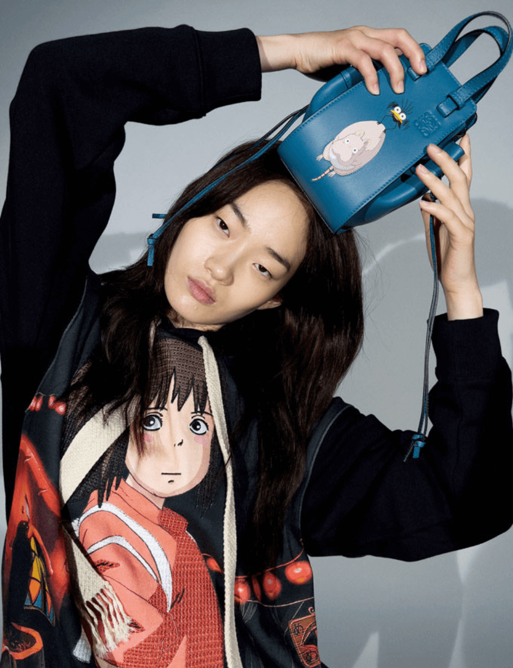 Loewe x A Viagem de Chihiro - tricot estampado preto e bolsa azul - Anime - inverno - mulher asiática posando segurando uma bolsa azul pequena na cabeça - https://stealthelook.com.br