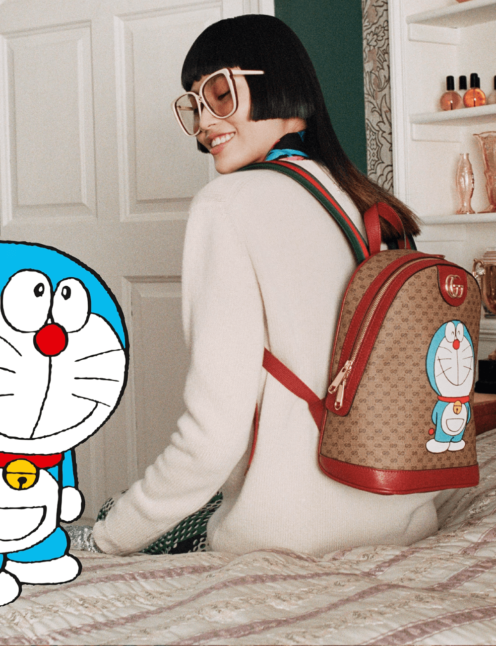 Gucci x Doraemon - roupas diversas - Anime - outono - mulher asiática de óculos sentada em uma cama de costas usando uma bolsa estampada com um desenho azul - https://stealthelook.com.br