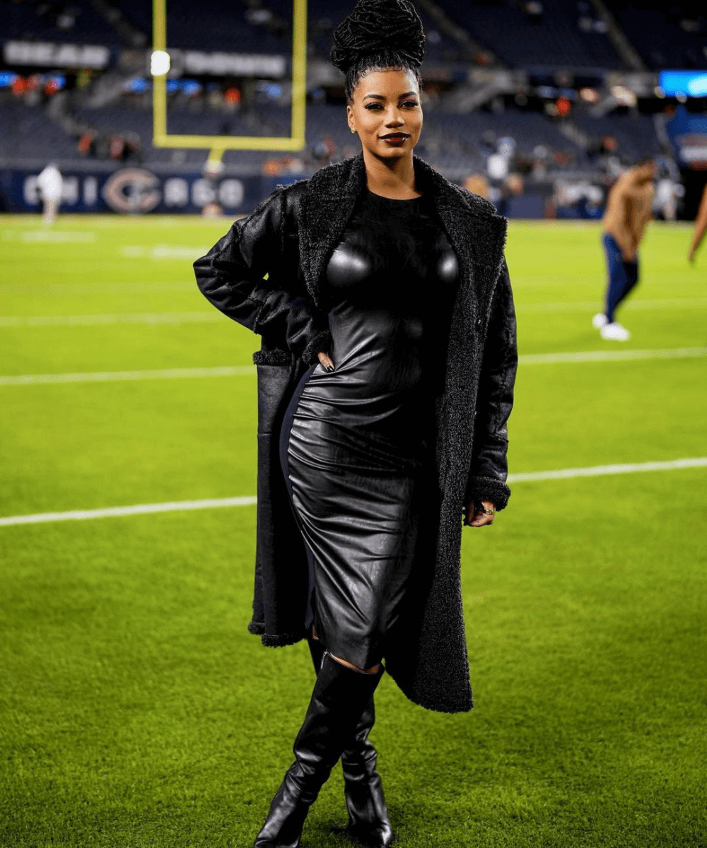 Taylor Rooks - vestido longo preto, bota preta e casaco preto - Taylor Rooks - inverno - mulher negra em pé em um campo de futebol americano - https://stealthelook.com.br