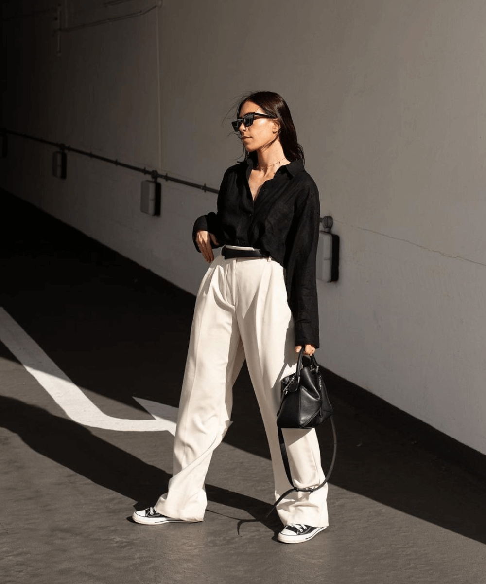 Jessica Skye - calça de alfaiataria branca, camisa preta e all star - All Star - outono - mulher em pé na rua usando óculos de sol - https://stealthelook.com.br