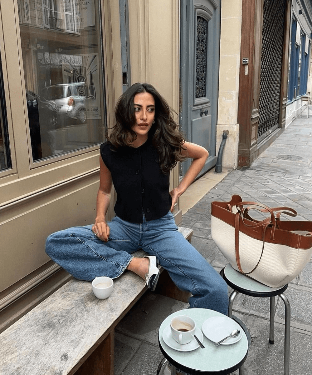 Taïna Cassagnes - calça jeans, colete preto e sapatilha - Easy chic - verão - mulher sentada em um banco na rua - https://stealthelook.com.br