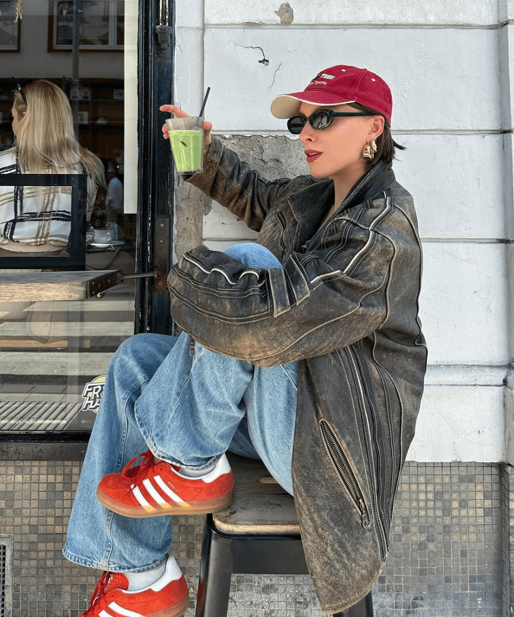 @lara_bsmnn - calça jeans, jaqueta de couro marrom, boné e óculos oval preto - óculos tendência - inverno - mulher de óculos e boné sentada em um banco na rua - https://stealthelook.com.br