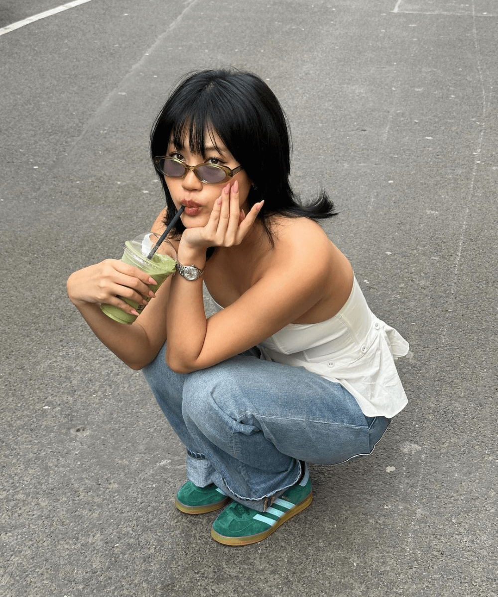 Jihoon Kim - calça jeans, blusa branca e óculos oval verde - óculos tendência - verão - mulher asiática agachada na rua tomando suco - https://stealthelook.com.br