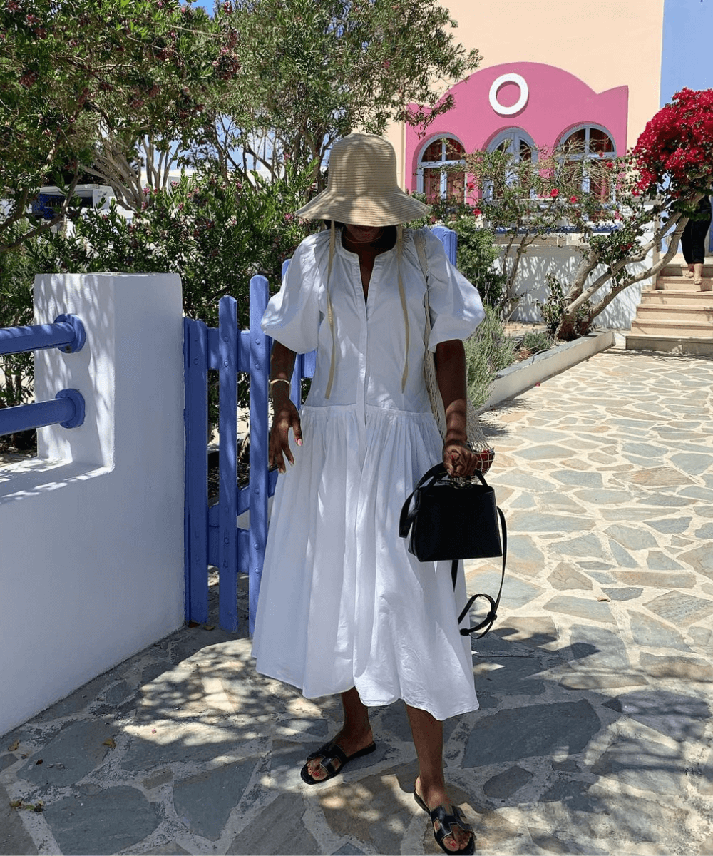 @taffymsipa - vestido midi branco bufante, chapéu, rasteirinha bege - vestido estiloso - primavera - mulher negra em pé na rua usando um chapéu de palha - https://stealthelook.com.br