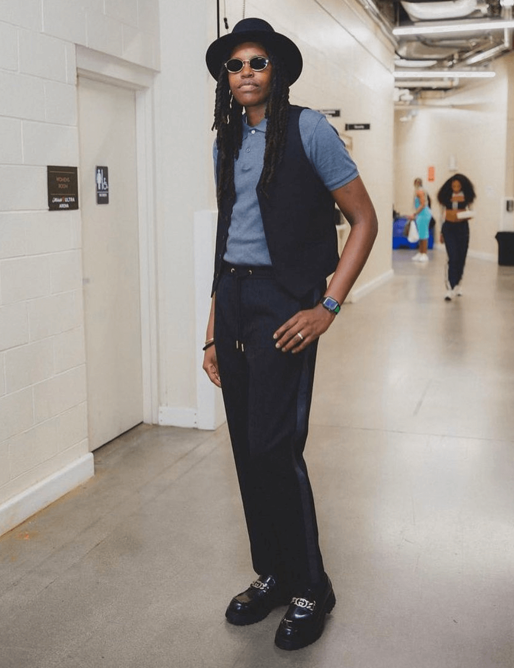 Jonquel Q Jones - calça preta, blusa polo, colete preto, óculos, chapéu e botas - WNBA - outono - mulher negra de chapeu e óculos em pé - https://stealthelook.com.br