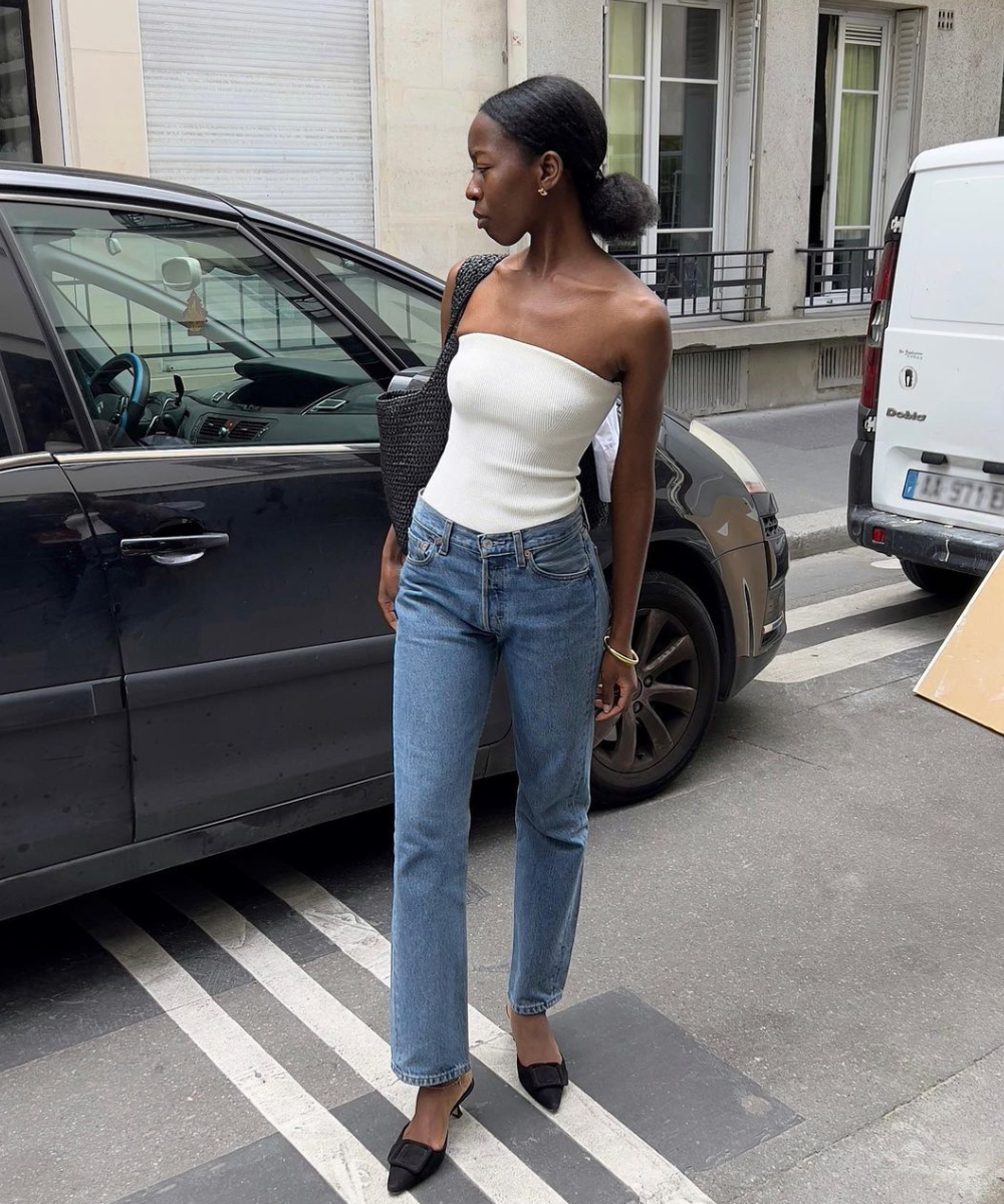 Sylvie Mus - calça jeans reta, top branco, kitten heels. Mulher negra parada em pé na rua usando um look básico