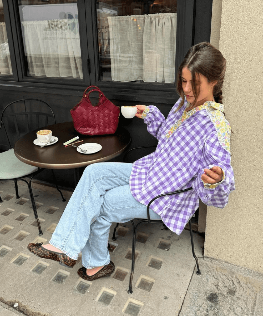 Manon De Velder - calça jeans, sapatilha de oncinha e camisa xadrez lilás - looks para festa junina com calça jeans - inverno - mulher sentada em um café na rua - https://stealthelook.com.br