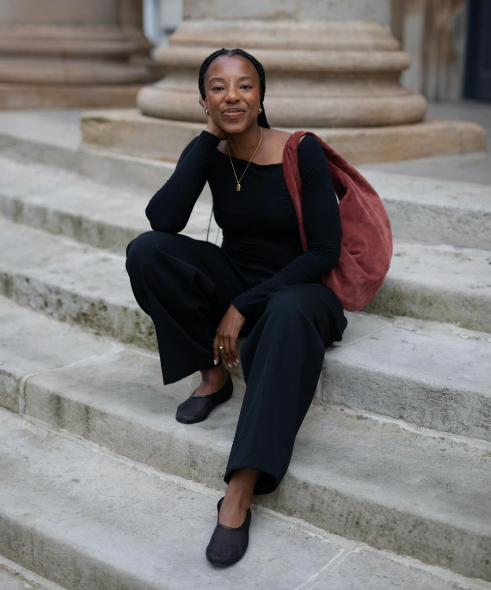 @taffymsipa - calça preta, blusa de manga longa preta, sapatilhas pretas e bolsa vermelha - looks com calça preta - outono - mulher negra sorrindo sentada em uma escada na rua - https://stealthelook.com.br