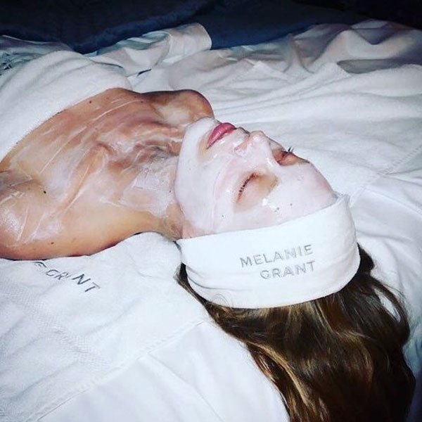 Pessoa em tratamento de SPA, deitada usando máscara facial branca. Usa tiara e toalhas brancas personalizadas com o nome 