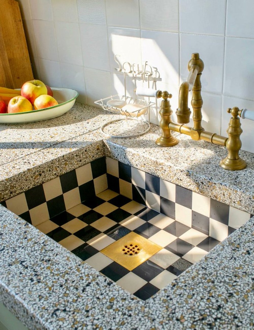 Pias de cozinha estilo vintage com cuba de azulejos preto e branco em padrão xadrez. Torneira de latão em design clássico. Bancada com acabamento de pedra agregada, detalhes retrô sofisticados.