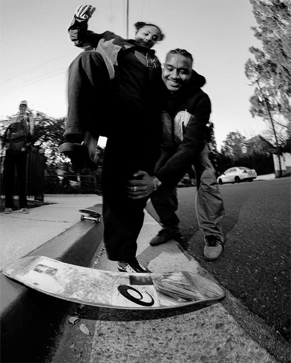 Imagem em preto e branco de pessoas praticando skate na rua. As roupas são estilosas e descontraídas, típicas da moda streetwear, incluindo calças largas, moletons e tênis. Os elementos refletem tendências urbanas e skaters, destacando conforto e estilo.