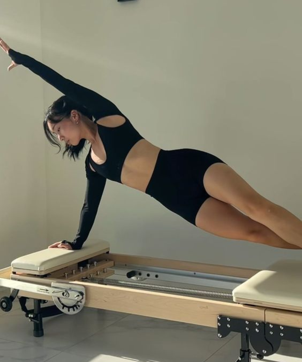 Pessoa treinando Pilates usando roupa esportiva preta composta por tops e shorts. O look destaca recortes estratégicos e manga longa em um dos braços, uma tendência moderna que combina estilo e funcionalidade para atividades físicas.