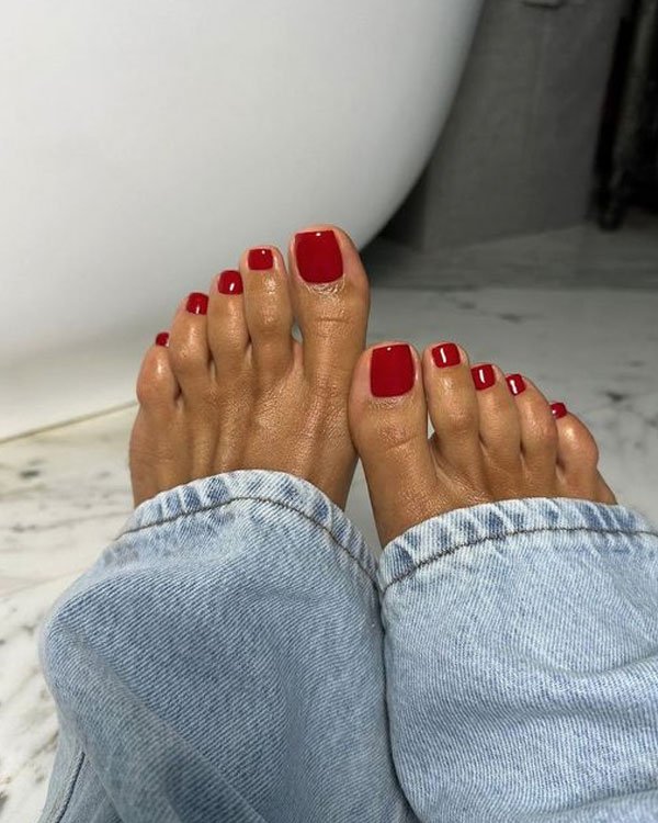 Unhas dos pés pintadas de vermelho intenso, tendência de moda em pedicure. Calça jeans ampla estilo vintage anos 90, realçando um look casual e despojado. Conforto e elegância em foco na moda cotidiana.