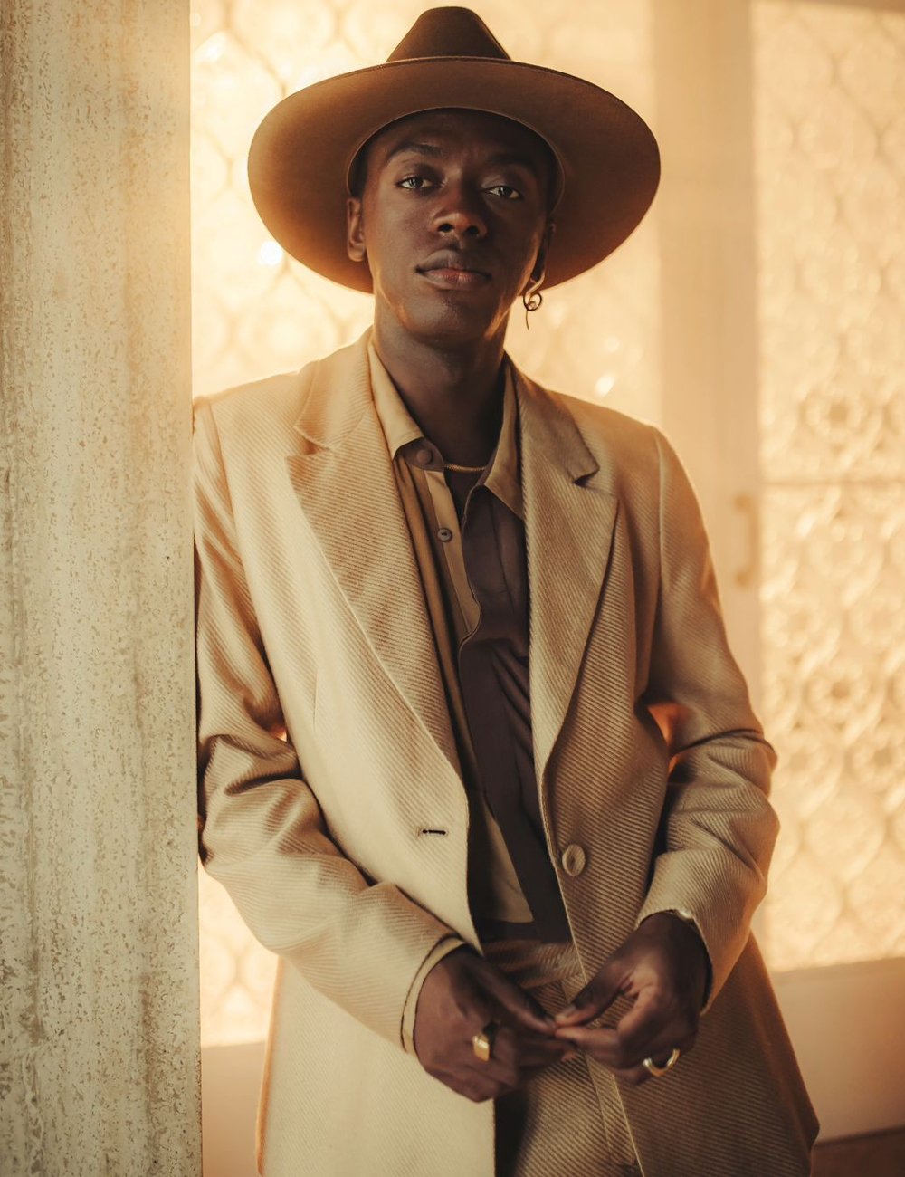 Homem elegante vestindo um terno bege com corte clássico e camisa em tons de marrom, combinando com um chapéu de aba larga de estilo western. Cantores brasileiros.