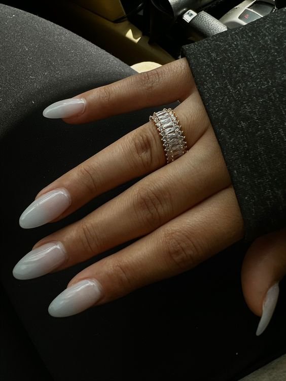 Mão feminina com unhas longas e pontiagudas bem cuidadas em tom branco opaco. Anel largo com pedras brilhantes em estilo elegante. Manga de blusa preta com tecido leve. Estilo moderno com tendências de moda minimalista e sofisticada.