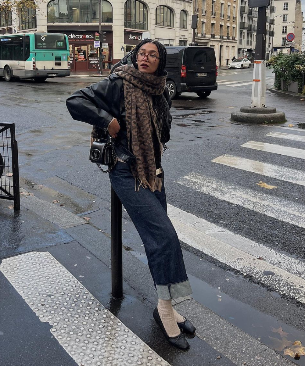 Moda de rua em Paris: jaqueta de couro preta, calça jeans dobrada, cachecol estampado, meias brancas e sapatos pretos. Estilo casual e chique com destaque para acessórios como bolsa e óculos de ar vintage.