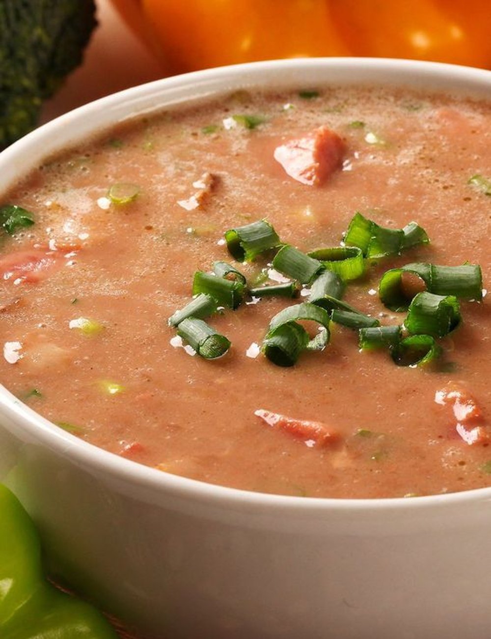 Imagem de uma sopa cremosa servida em uma tigela branca. A sopa, de aparência caseira, parece ser de feijão, decorada com cebolinha verde picada. Receitas para o frio.