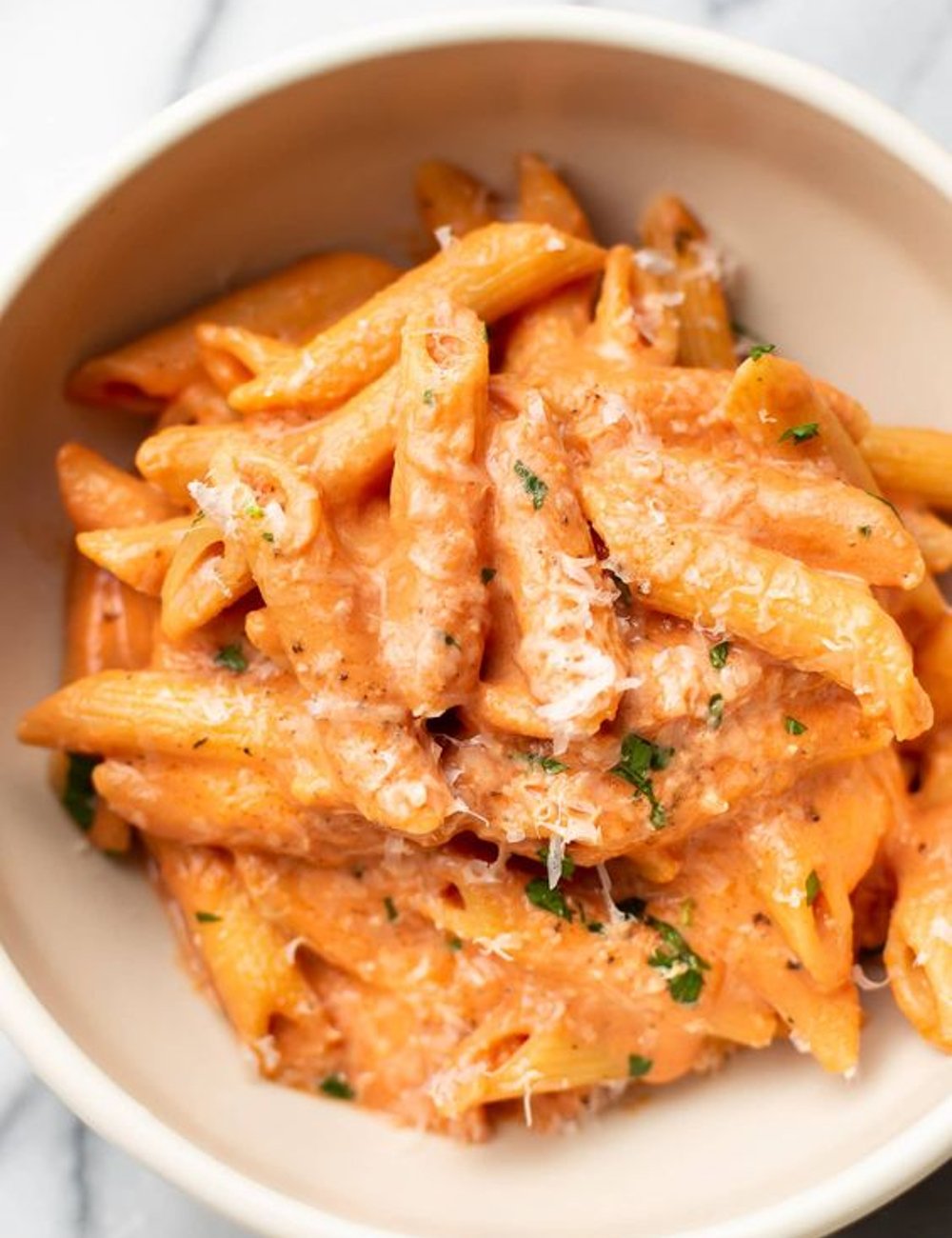 Imagem de um prato de penne ao molho rosé, coberto com queijo ralado e tempero verde. Pasta cremosa e apetitosa, ideal para amantes da culinária italiana. Receitas para o frio.