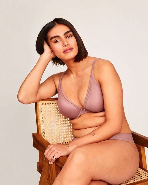 Modelo posando em ambiente minimalista, vestindo lingerie em tom nude. O estilo destaca conforto e naturalidade, alinhado à tendência de representatividade e inclusão no mundo da moda, promovendo corpos reais e autênticos.