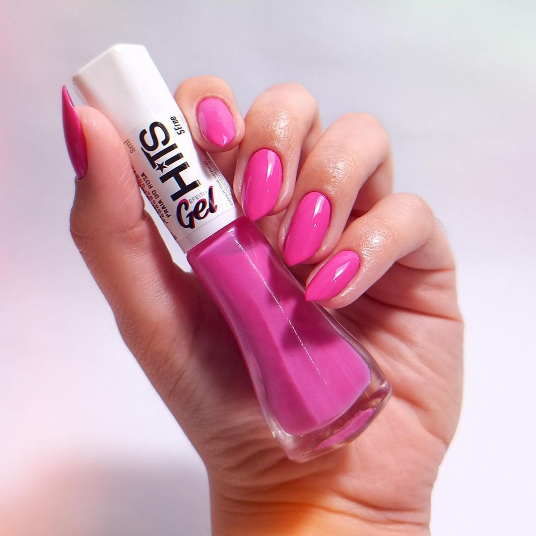 Esmalte rosa gel acetinado da marca Hits nas unhas. As unhas estão pintadas de rosa vibrante e têm formato ovalado, tendência atual na moda de nail art. Estilo moderno e feminino, ideal para quem busca sofisticação e cor nas unhas.