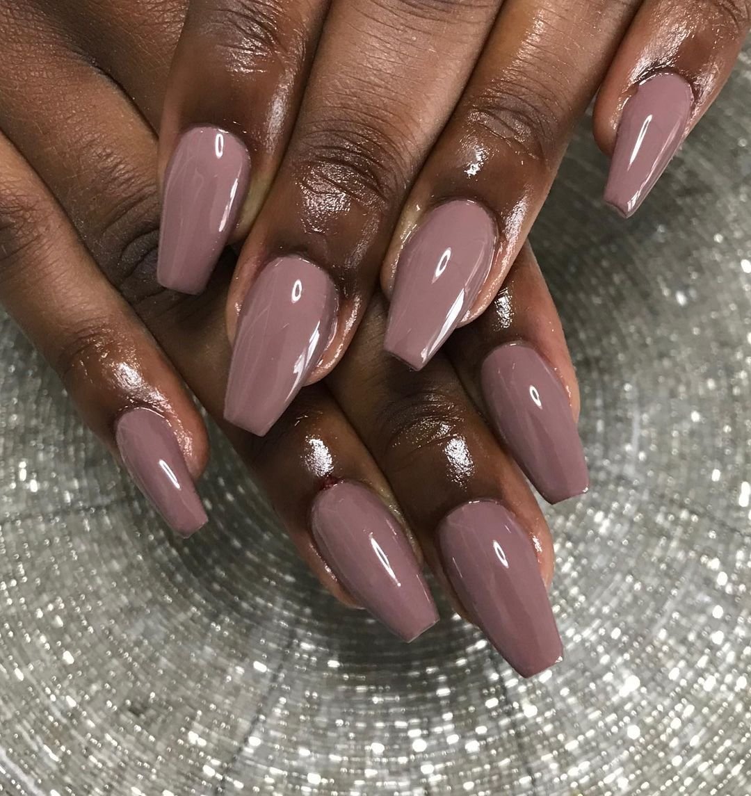 Unha bailarina longas e quadradas com esmalte marrom nude, destacando uma tendência minimalista e sofisticada. O acabamento brilhante reforça o estilo elegante e moderno, ideal para diversas ocasiões e combinando com diferentes estilos de moda.