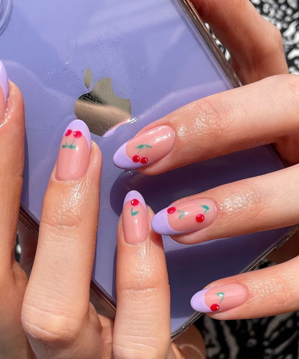 Unhas decoradas com detalhes de cerejas e pontas francesas lilás em fundo transparente. Design moderno e delicado que combina tendências de nail art e minimalismo. Ideal para um look jovem e despojado.