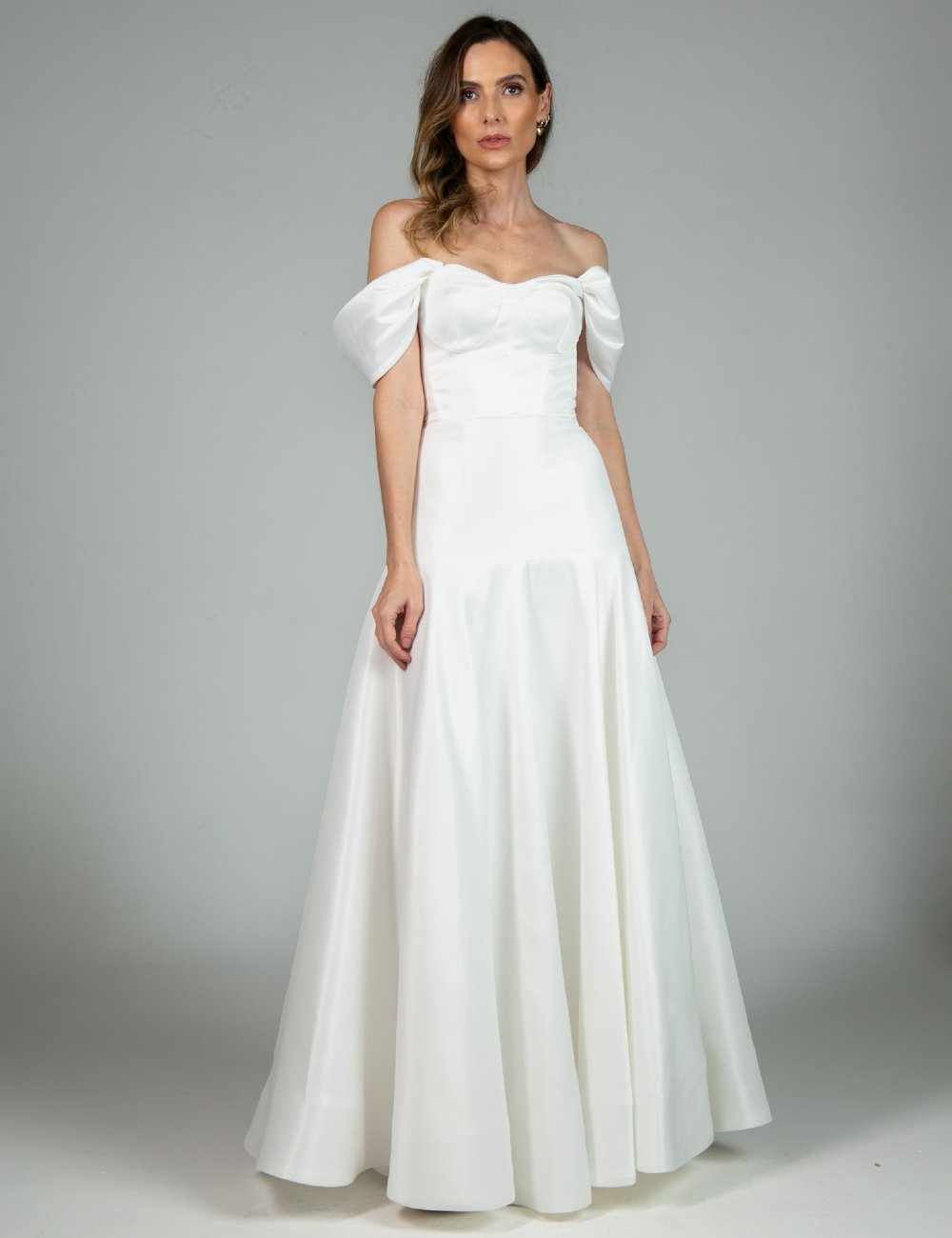 Vestidos de noiva clássico tomara que caia off-shoulder, com caimento elegante e volume na saia. A peça apresenta tendência de moda minimalista, misturando sofisticação e romantismo. Ideal para casamentos tradicionais.