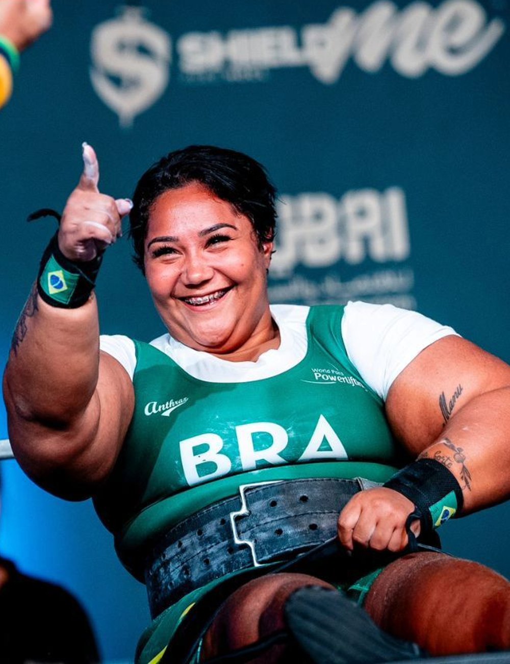 Atleta de halterofilismo usa uniforme verde e branco do Brasil com a palavra 