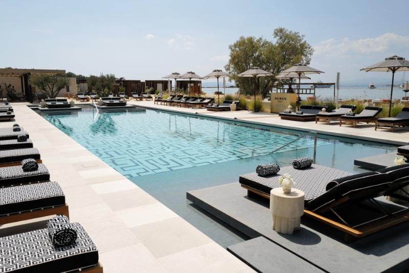 Piscina elegante em resort de luxo à beira-mar. Espreguiçadeiras com estofado em padrão geométrico preto e branco, chapéus de sol modernos e design minimalista. Ambiente sofisticado, ideal para relaxar e desfrutar de um dia ensolarado com estilo.