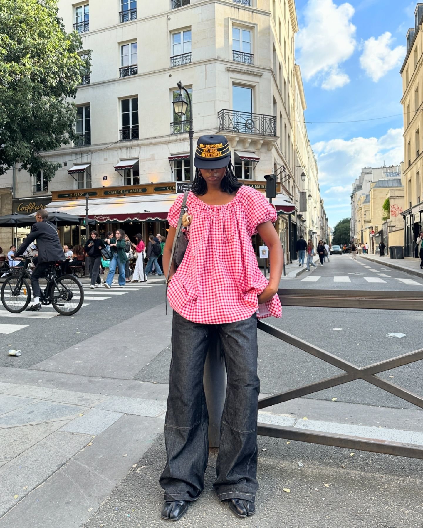 Pessoa vestindo blusa de estampa xadrez vermelho e branco, calça jeans larga e botas pretas.Destaque para o boné estilo militar. tendência: mistura de peças oversized com elementos de streetwear.