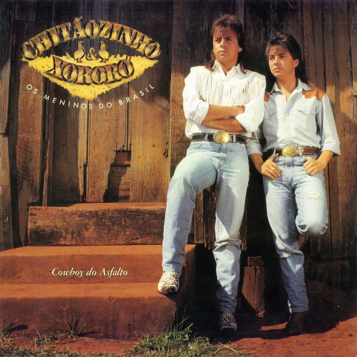 Música sertaneja anos 80: Camisas jeans de manga longa, cintos com fivelas grandes e botas country. Visual clássico de sertanejo urbano, destacando franjas e detalhes rústicos. Moda representativa do estilo sertanejo brasileiro.